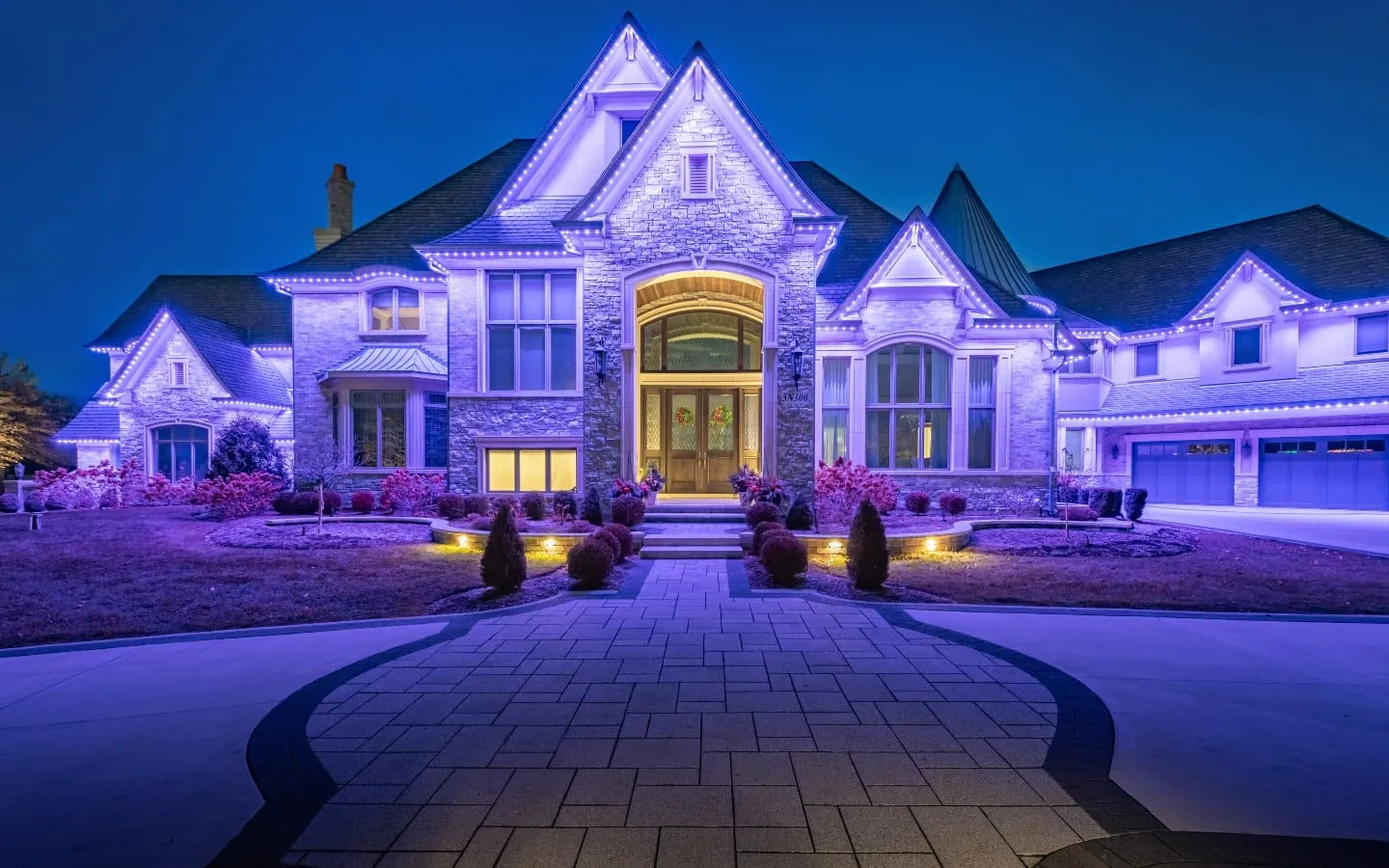 Luxury home outlined in blue accent lighting with warm landscape lighting at dusk