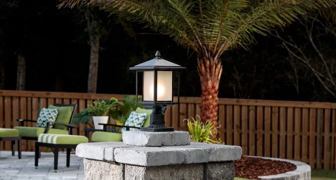 Craftsman-style post lantern glowing warmly on a stone pillar in the evening